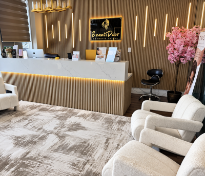 BeautiDoor Luxury Med Spa – Mississauga BeautiDoor reception with an illuminated front desk, gold-toned wall panels, cream seating and a pink floral arrangement.