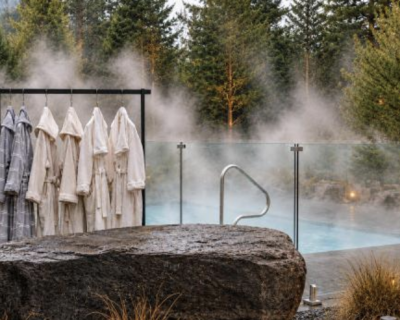 DERM Nordic Spa at Nomi Resort – Outdoor Thermal Pool Steam rising from an outdoor thermal pool surrounded by trees, with bathrobes hanging nearby at DERM Nordic Spa.